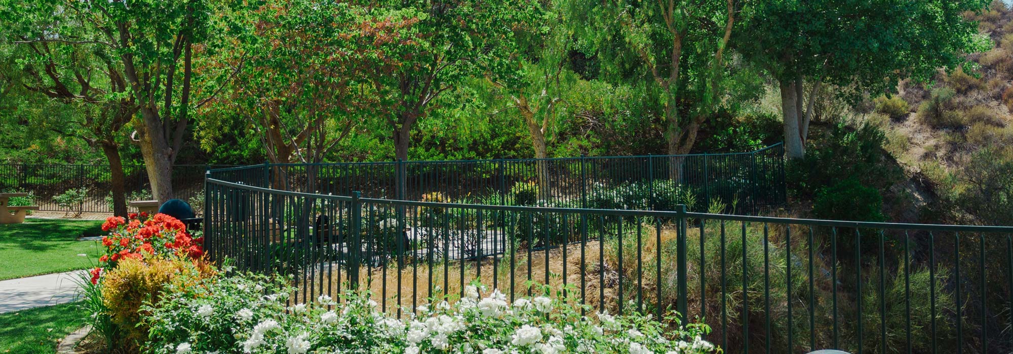 wrought iron fence in a garden with trees, flowers and grass